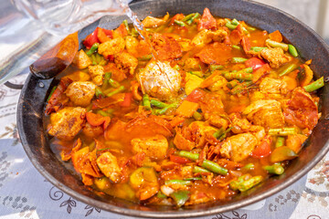 Chef pouring water into paella with chicken, chorizo and green beans