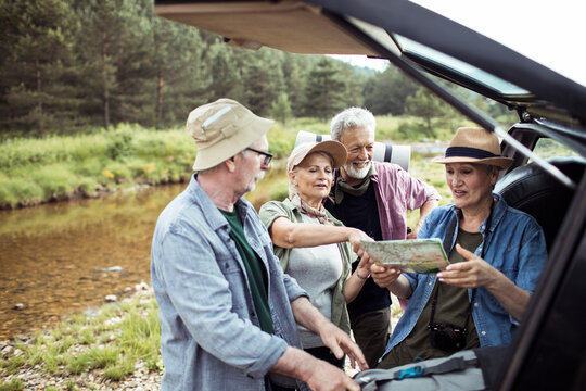 Senior friends planning hiking route with map near car by river