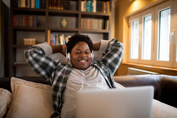 Smiling young man relaxing on the couch with headphones and laptop at home
