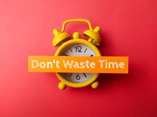 Alarm clock and sticky note with the word Dont waste time on red background