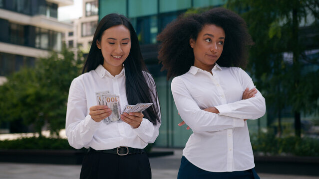 Asian Korean African American women count money salary bonus income envy arms crossed females inequality business financial colleague rivalry jealousy cash pay bills discrimination girls rich outdoors