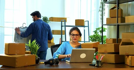 Indian Asian small businesswoman and businessman engaged in routine warehouse chores like verifying product checklist, doing data entry, and preparing packed carton boxes for export shipment dispatch