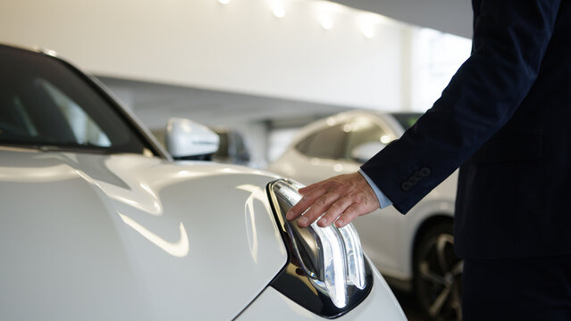 Unrecognizable man touching car dealership automobile headlight buyer stroking vehicle showroom review new auto store male businessman choose salon client transport choosing dreaming business customer