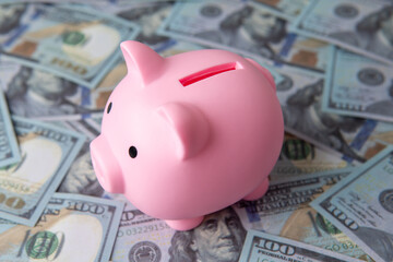 A piggy bank on a bed of blurred one hundred U.S. dollar bills. Business and finance concept.