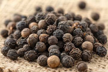 A close-up photo of black pepper grains scattered on a white surface, creating a textured and flavorful culinary ingredient.