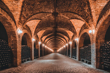 Fototapeta premium Majestic wine cellar with brick arches, rows of aging wine bottles, and soft lighting creating a captivating atmosphere.