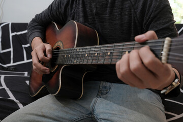 Close-up of man's hands playing acoustic guitar at sofa home. Fingers skillfully strumming strings, creating melodic sounds, music hobbies