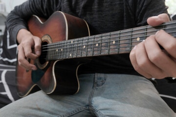 Fototapeta premium Close-up of man's hands playing acoustic guitar at sofa home. Fingers skillfully strumming strings, creating melodic sounds, music hobbies