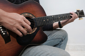 Close-up of man's hands playing acoustic guitar at sofa home. Fingers skillfully strumming strings, creating melodic sounds, music hobbies
