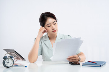 Professional ponders over documents at her desk clock ticking highlighting focus on details