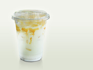 front view white and yellow caramel milk in a clear plastic glass on white and cream background, drink, milk, sweet, copy space