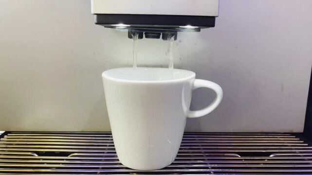 A modern automatic coffee machine is punching hot espresso. Foam and steam are coming out. Slow motion 