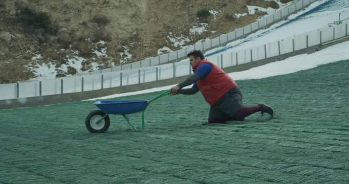 Grown man doing weird stretching routining with wheelbarrow at bottom of olympic ski ramp - slow motion 