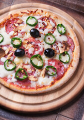 Pizza with salami and mozzarella cheese, jalapeno pepper and black olives. Wooden background. Soft focus. Close up.	