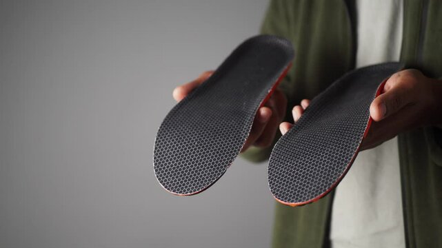 Shoe insoles displayed by a person in a neutral background