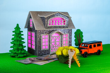 On a light background with pink light in the windows, a gray house surrounded by an orange car with flowers and keys and euro and dollar banknotes