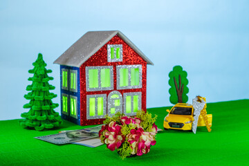 On a light background with light green light in the windows, a red and blue house surrounded by a yellow car with keys and euro and dollar banknotes
