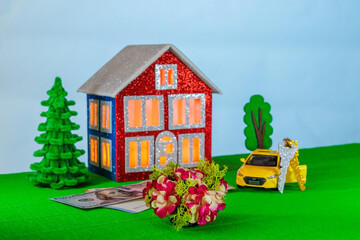 On a light background with orange light in the windows, a red and blue house surrounded by a yellow car with keys and euro and dollar banknotes
