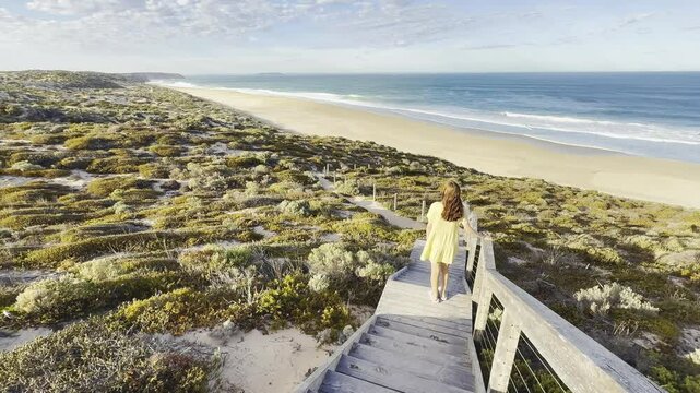 girl stands on wooden stairs and admires long sandy beach between west cape lookout and Ethel Wreck Beach with powerful waves. Dhilba Guuranda-Innes National Park, Yorke Peninsula, south australia