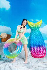 Asian Model in Green Bikini Holding Rainbow Float and Smiling