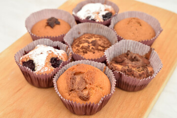 Different homemade muffins with chocolate, cocoa powder, jam and sour cherry sprinkled with powdered sugar on the wooden board. Close-up. Selective focus.