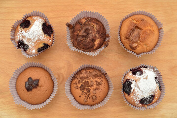 Different homemade muffins with chocolate, cocoa powder, jam and sour cherry sprinkled with powdered sugar on the wooden board. Top view.