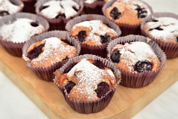 Homemade muffins with sour cherry sprinkled with powdered sugar on the wooden board. Close-up. Selective focus.