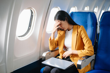 Photo of a frustrated woman sitting on an airplane with her head in her hands. Asian woman sitting