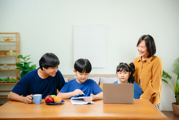 Homeschool Asian young little boy learning online and does homework by using computer and tablet with mother help, teach and encourage.