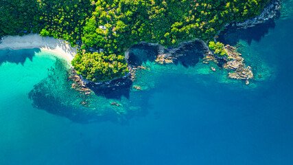 A breathtaking aerial view of a secluded Freedom beach with crystal-clear turquoise waters, surrounded by lush green vegetation and rocky cliffs. The pristine white sand and vibrant ocean hues