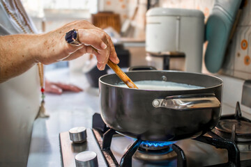 Senior woman stirring hot milk with wooden spoon on gas stove