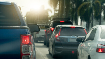 Rear side of blue pickup car with turn on brake light. Many car queue up due to traffic congestion. Side road with trees. Background of bright light of the sun shines.