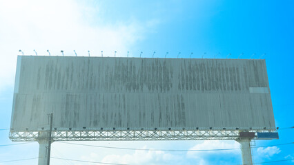 Blank billboard against a bright blue sky with some clouds. Billboard is supported by metal beams and posts. Suggesting it ready for advertising. Junction of No 3 Road of Chanthaburi Thailand.
