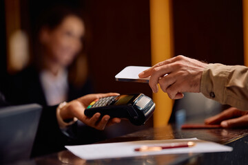 Close up of man paying with mobile phone at hotel reception desk.