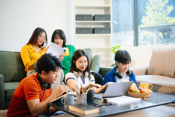 Group of young Asian students working on a project with laptops and tablets. Cozy indoor setting, teamwork,