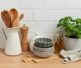 Kitchen utensils, bowls and spices resting on wooden countertop with white brick wall background