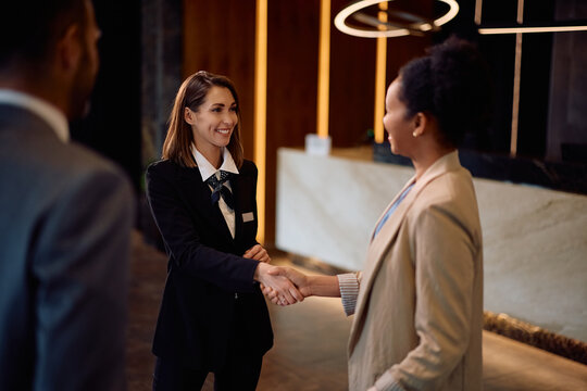 Happy female concierge greeting a business couple in hotel lobby.