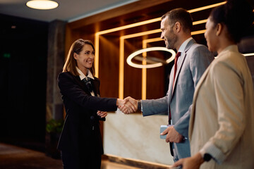 Happy female concierge greeting business couple in hotel lobby.