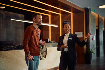 Happy black hotel manager welcoming her guest in lobby.