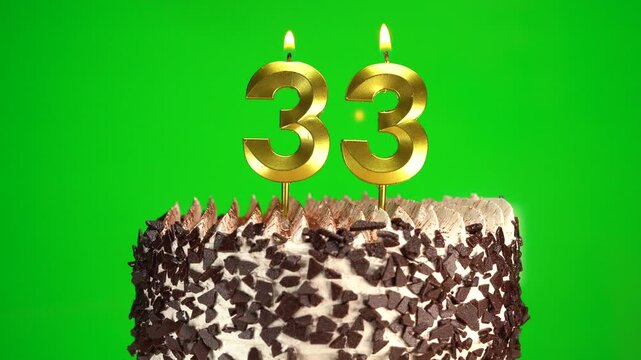 Lighting candles on Chocolate birthday cake on green chroma key background with number thirty-three golden candles. Celebration Birthday cake for 33 years.