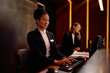 Happy black hotel manager using desktop PC while working at reception desk.