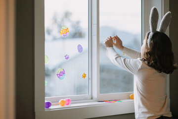 Child decorating window with Easter stickers and eggs.