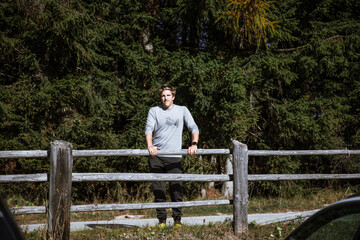 Fototapeta premium Man leaning on wooden fence in South Tyrol forest