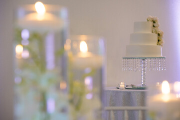 Elegant white wedding cake with candles in soft focus foreground