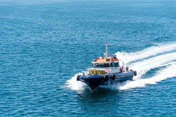 Pilot boat sailing across calm, blue waters on her way to assist a cargo ship during arrival maneuverings to the port terminal. Jebel Ali - United Arab Emirates.  