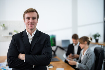 Young professional in business attire smiles confidently in modern office during team meeting in progress