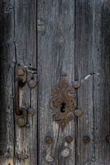 Close-up of an old weathered wooden door with an ornate rusted metal lock and textured grain. Vintage, rustic detail with strong character and patina.