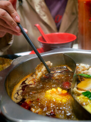 human hand using chopsticks hold meat over Sichuan mala hotpot shabu on restaurant table.