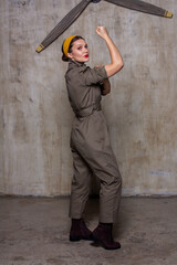 Person in beige jumpsuit yellow headband burgundy boots against textured wall