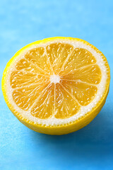 Half a lemon with visible texture on pastel blue background, symbolizing freshness and citrus energy